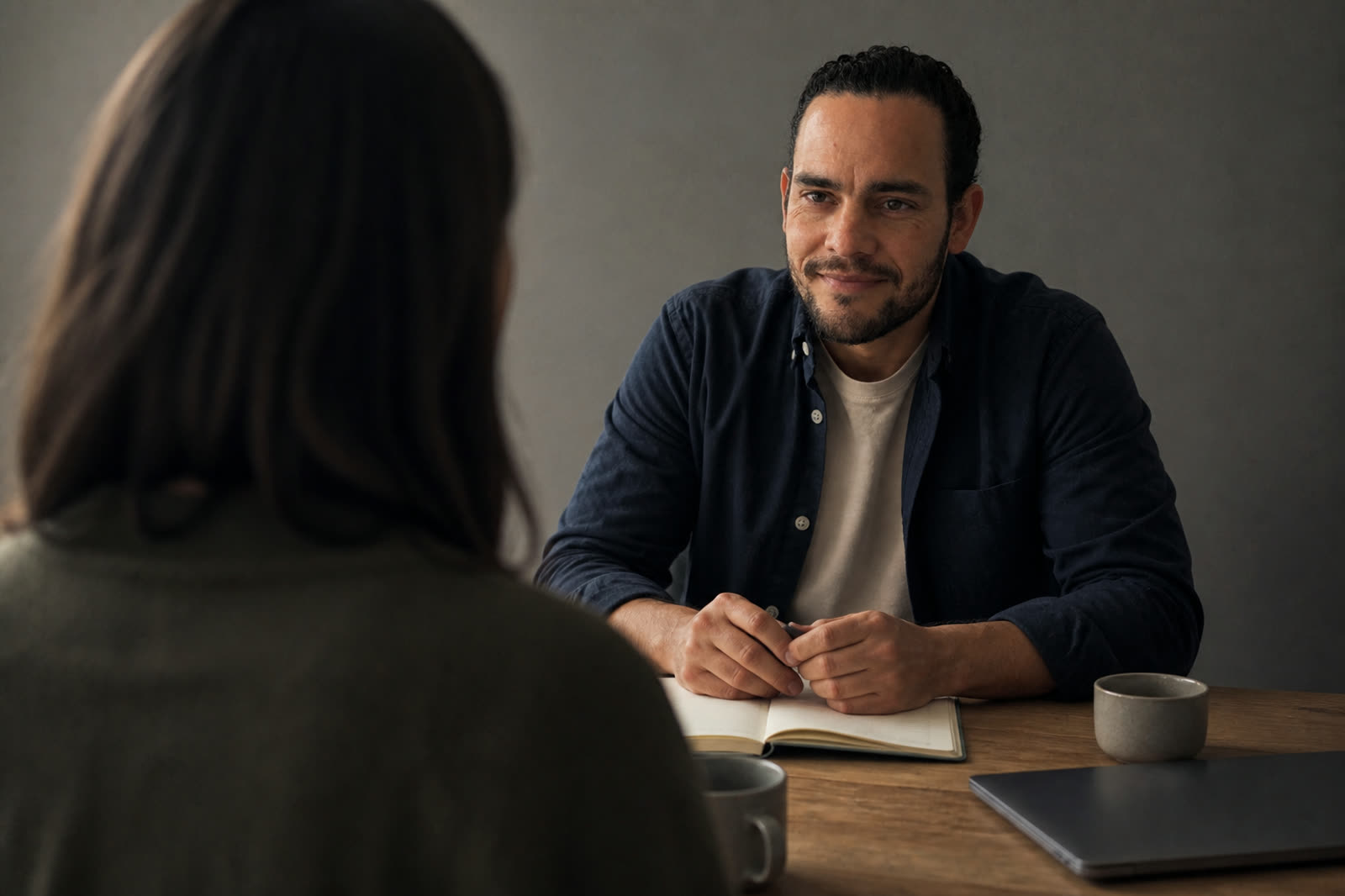 Two people talking across a wooden table in natural light.